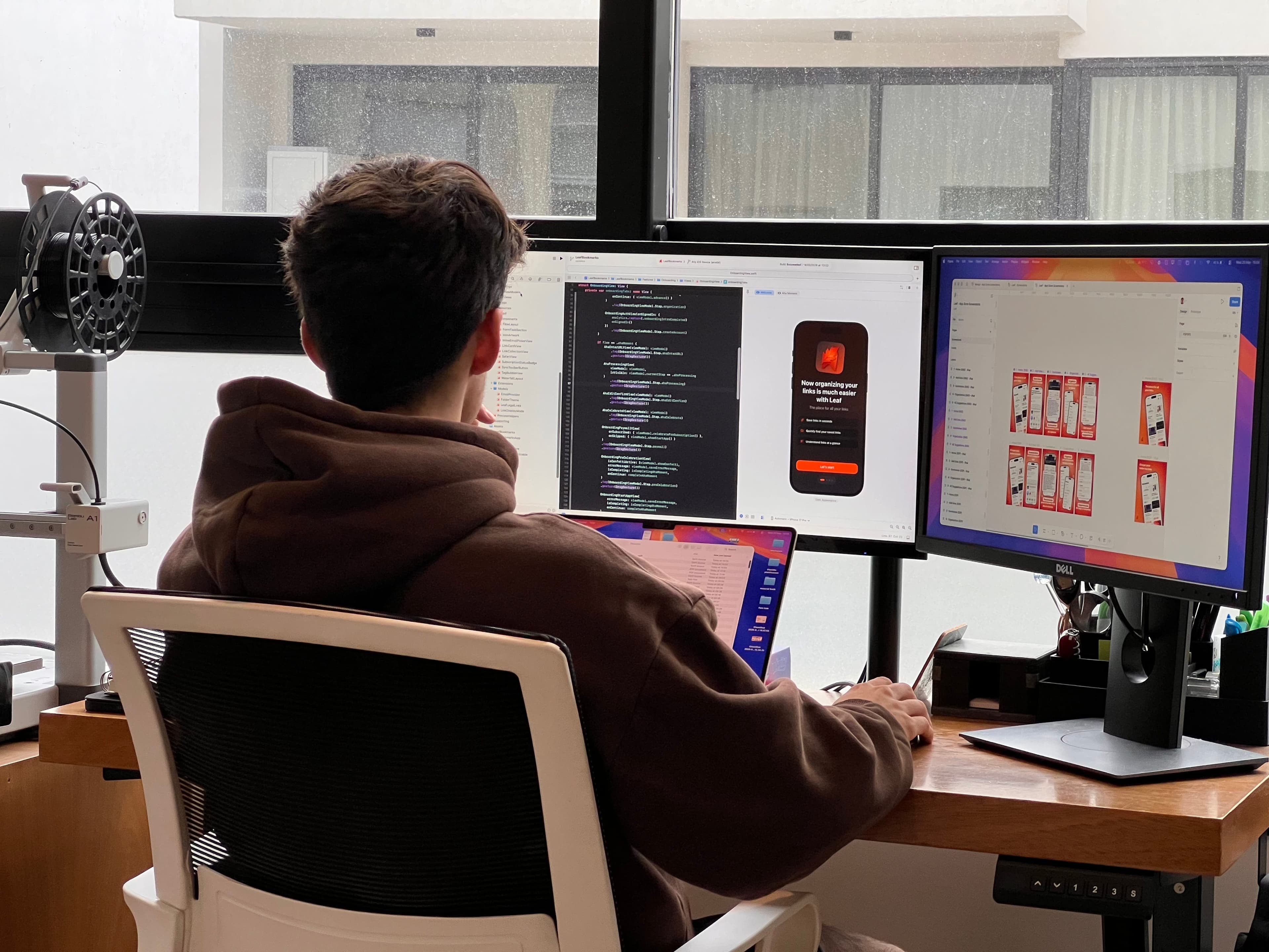 Tomás trabajando frente a dos monitores con código y diseños de una app